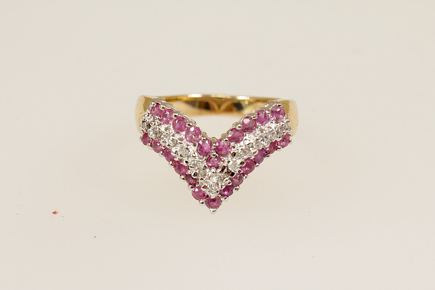 This beautiful 9ct Gold cluster ring is designed in a wishbone shape; featuring 3 bands of gemstones, creating a striking and meaningful design. The two rows of round-cut rubies (24 in total) bring a vibrant deep red colour, symbolising passion and prosperity, while the central row of diamonds adds a touch of brilliance and contrast, enhancing the overall sparkle. The London hallmarks for 1992, UK finger size M.