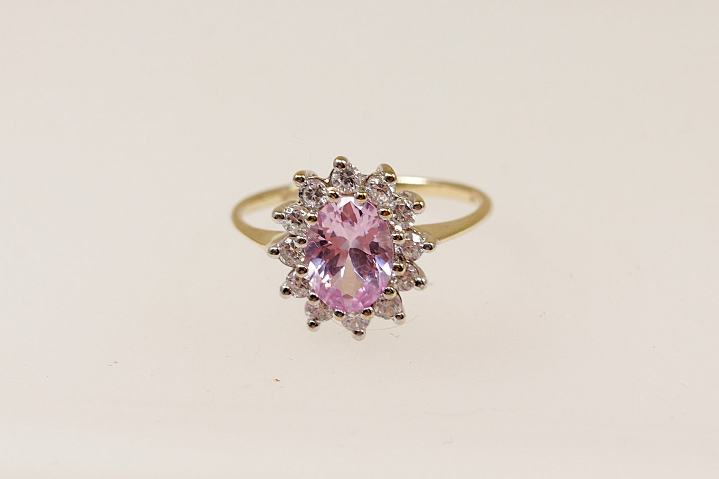 A 9ct gold ring with an oval pink sapphire centerpiece and a halo of round-cut cubic zirconia around it.