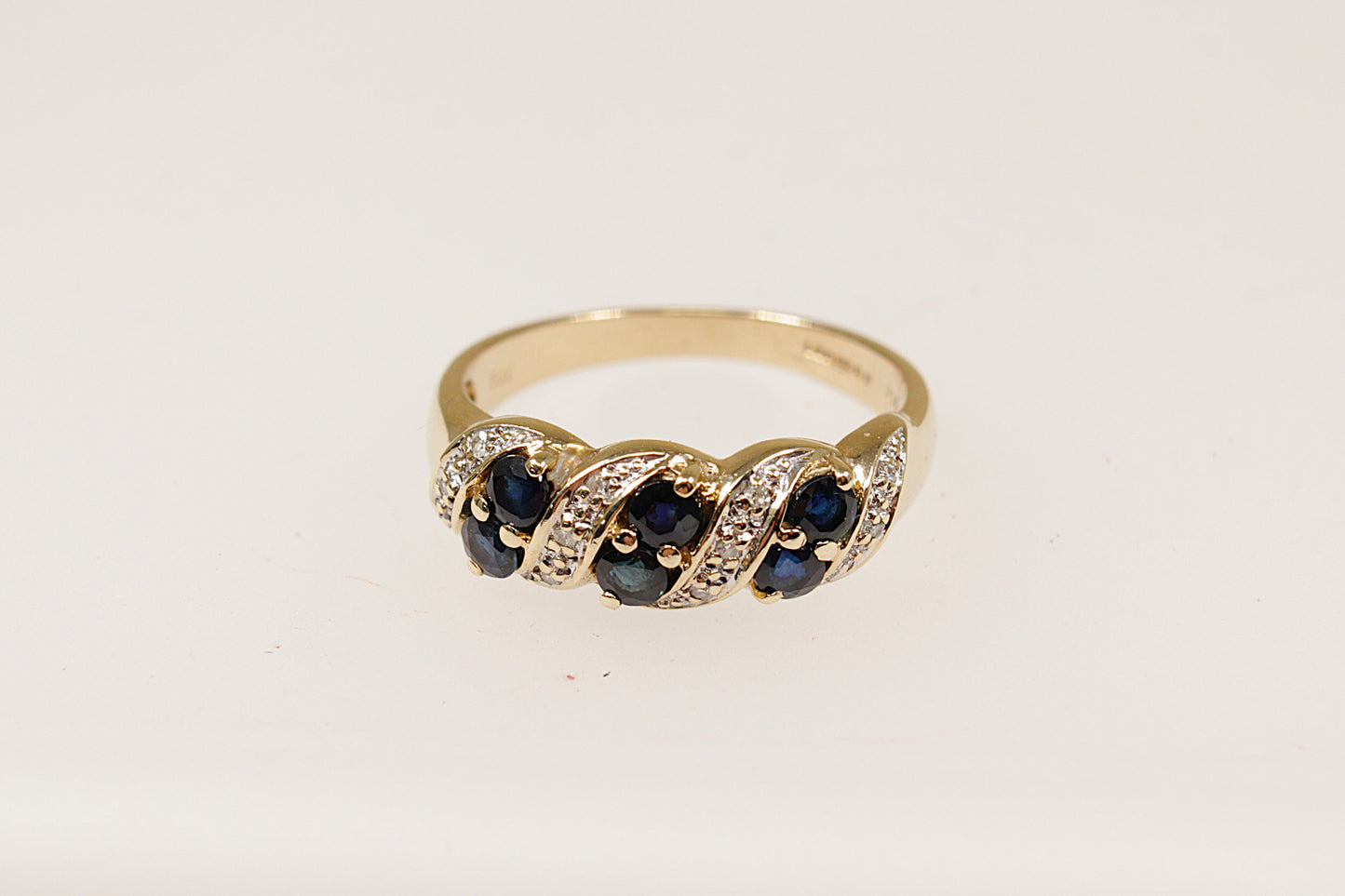 A 9ct gold ring featuring a slanted arrangement of round sapphires with diamond accents, claw set on the band.