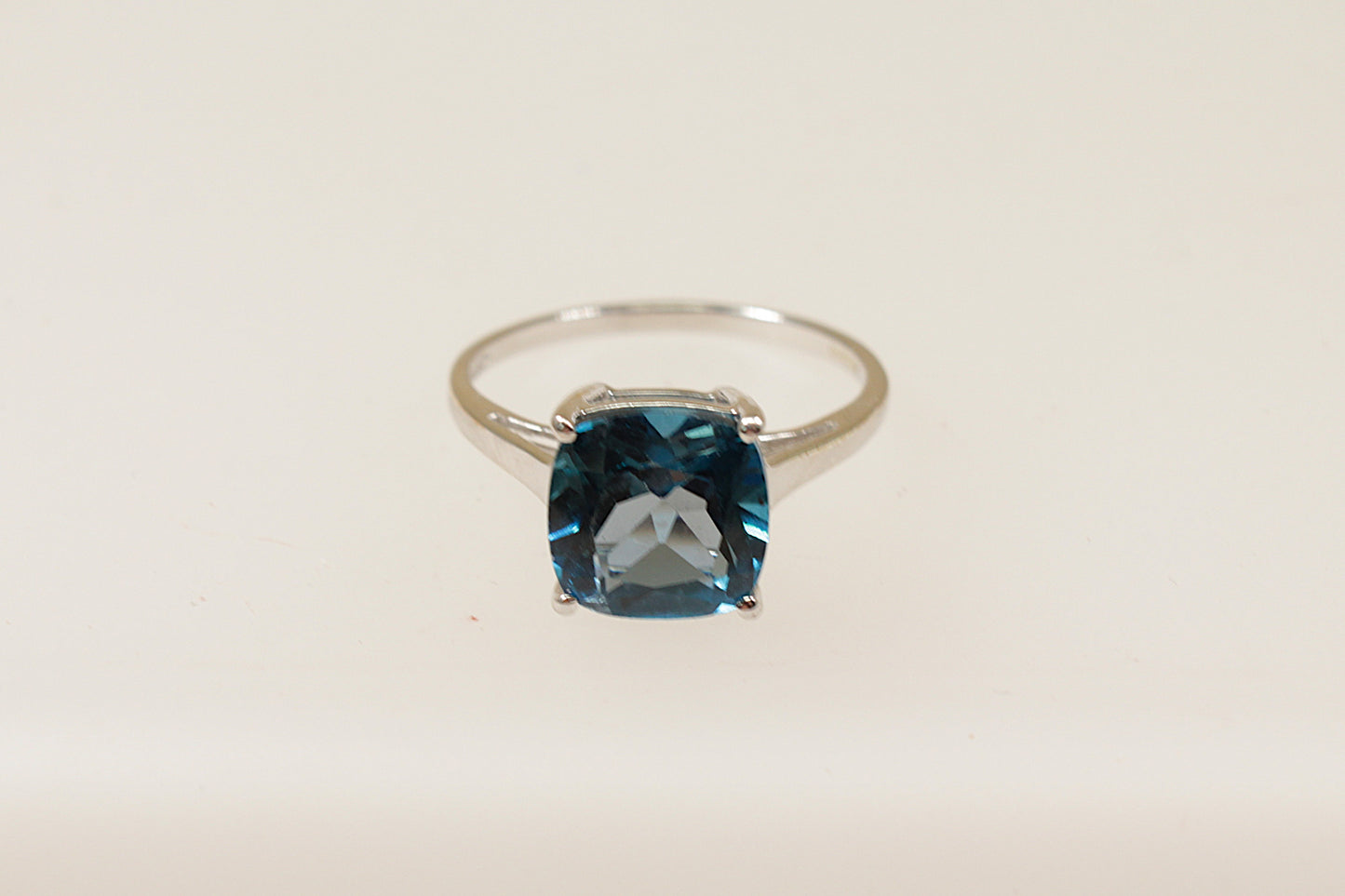 A 9ct white gold solitaire ring with a cushion cut London Blue Topaz held securely in a crown setting with four claws.