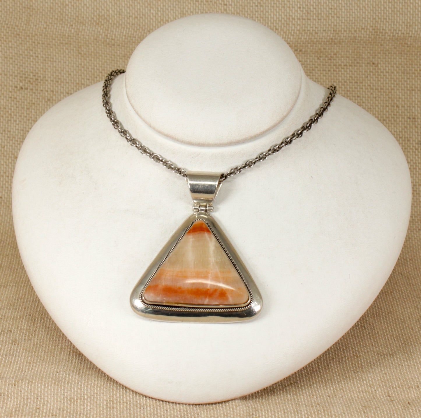A triangular sterling silver pendant with a pinky / brown agate gemstone, mounted on a white display stand.