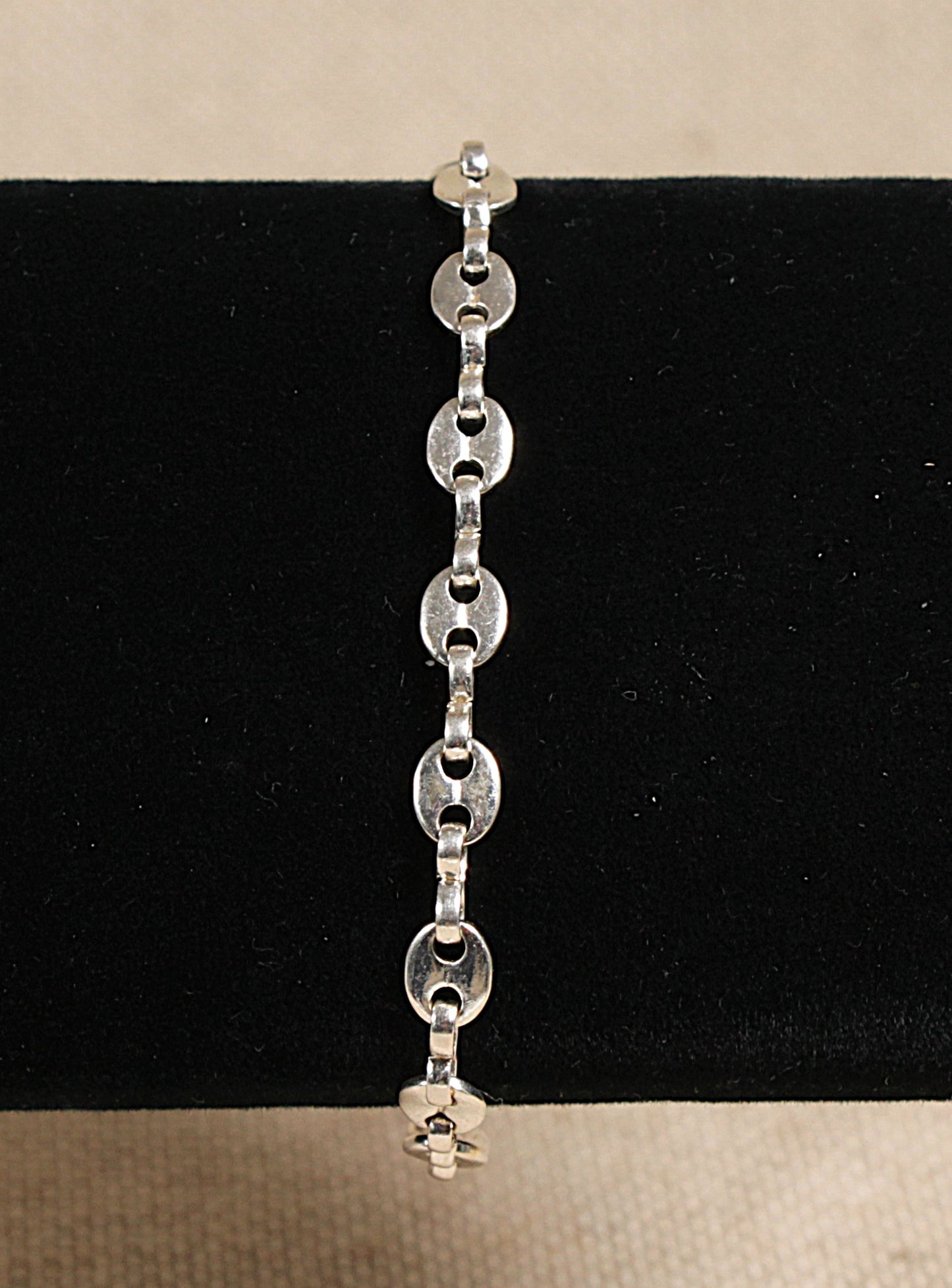 A silver anchor chain link bracelet with a lobster clasp fastening, displayed against a black background.