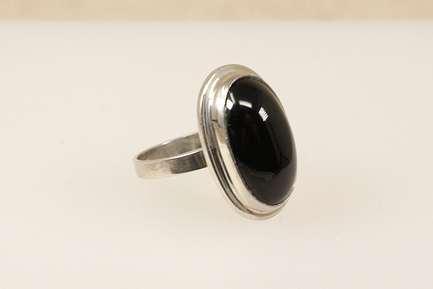A silver ring with a large oval black cabochon stone set in a solid bezel, on a white background.