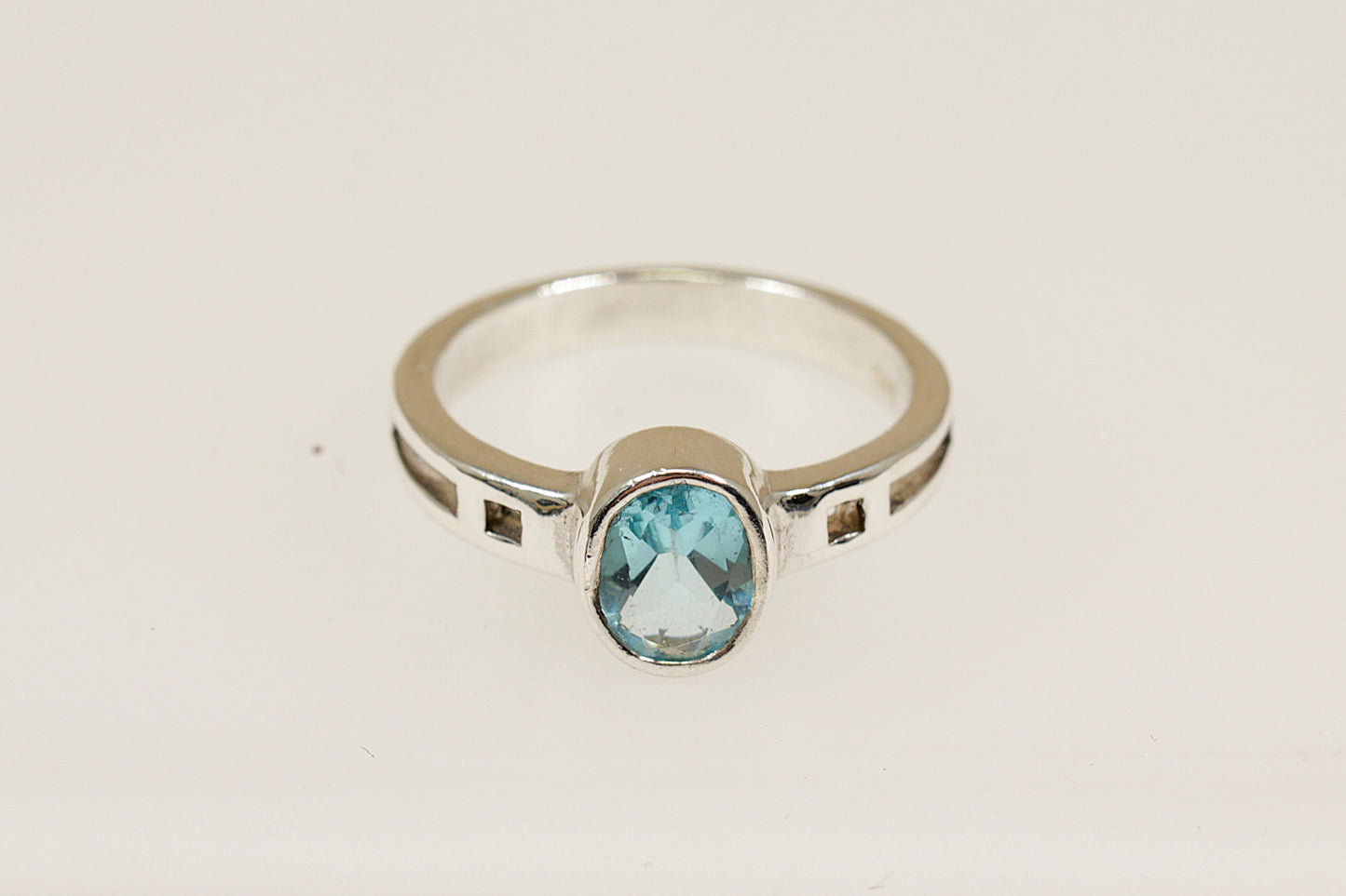 A silver ring with an oval blue faceted crystal set in a bezel, with geometric cut-outs on the shoulders.