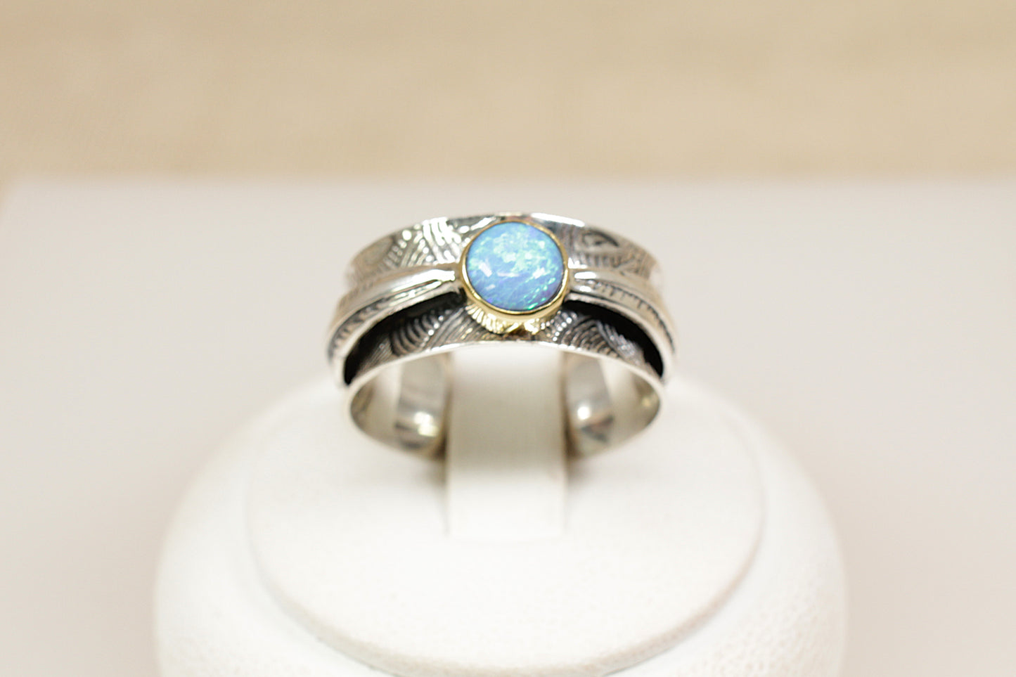 A sterling silver ring with a round blue opal gemstone in a bezel setting, featuring a nature-inspired fan or leaf design on the band.