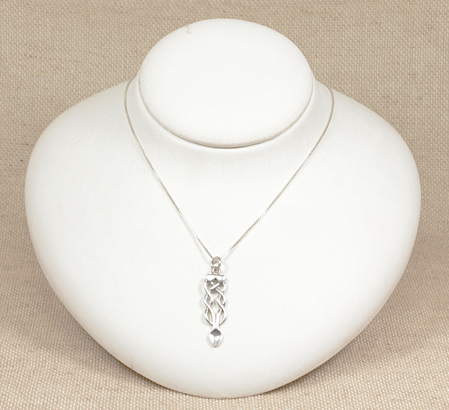 A silver Celtic knot pendant necklace displayed on a white mannequin bust against a beige background.