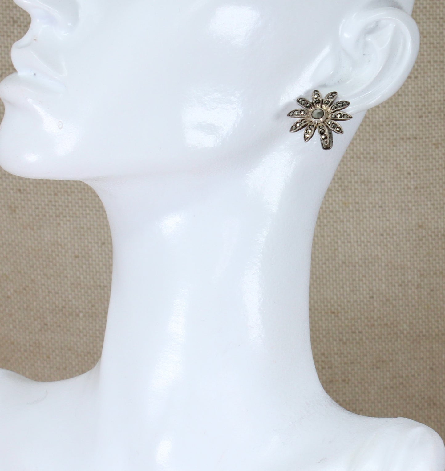 A pair of silver clip-on earrings with marcasite encrusted in a floral pattern displayed on a mannequin head.