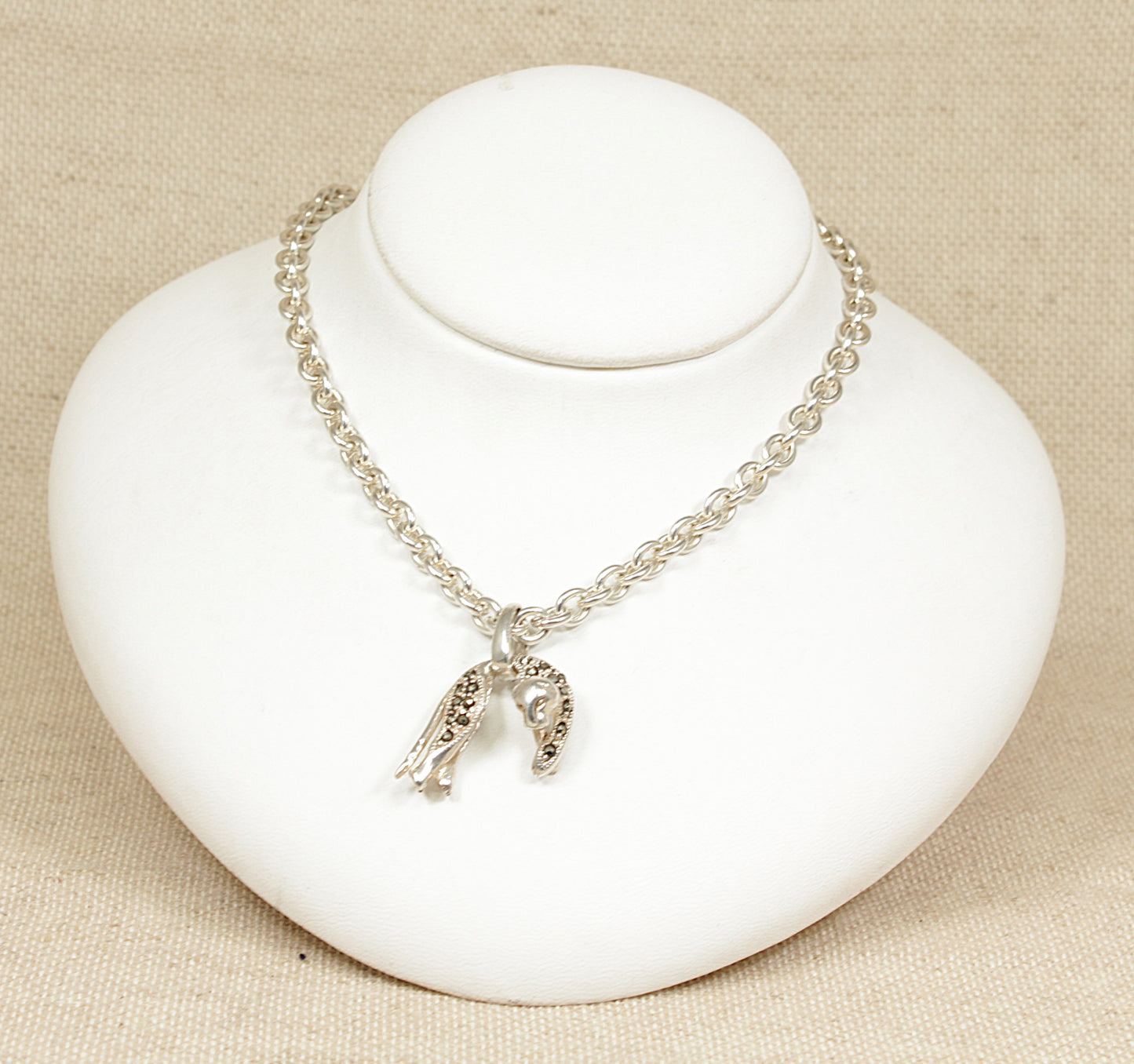 A silver necklace with a leopard pendant and two heart charms displayed on a white mannequin.