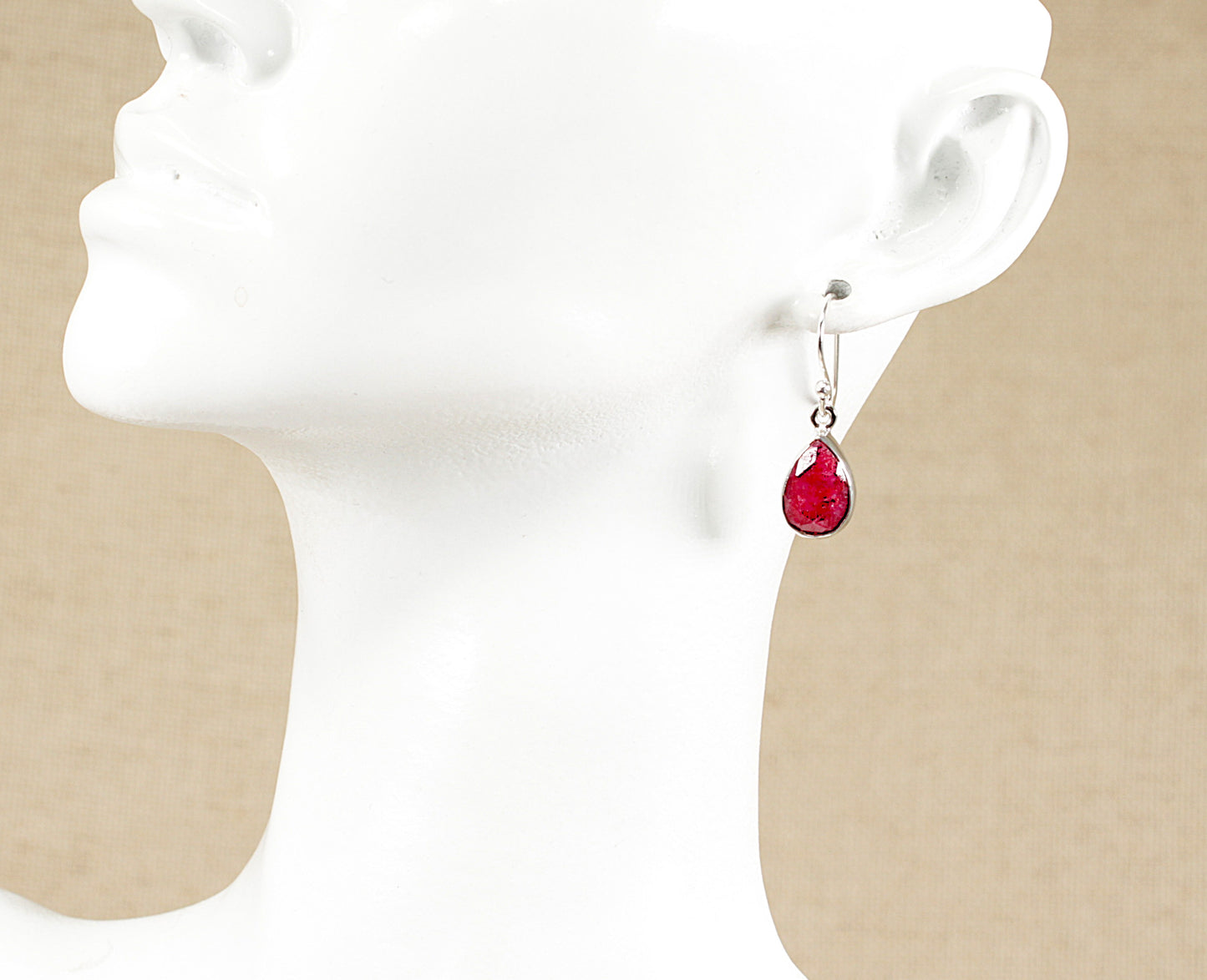 Red teardrop earrings on a white mannequin head with beige background