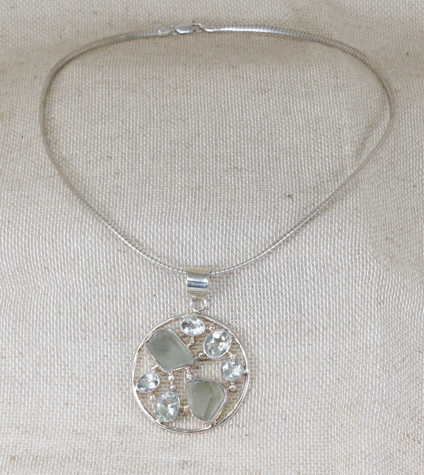 This gorgeous Silver collarette has a large round handcrafted pendant inset with faceted and raw Quartz gemstones in an asymmetric design. Made in Italy, this statement pendant sits on a snake chain collarette. Pendant size: 42mm round.