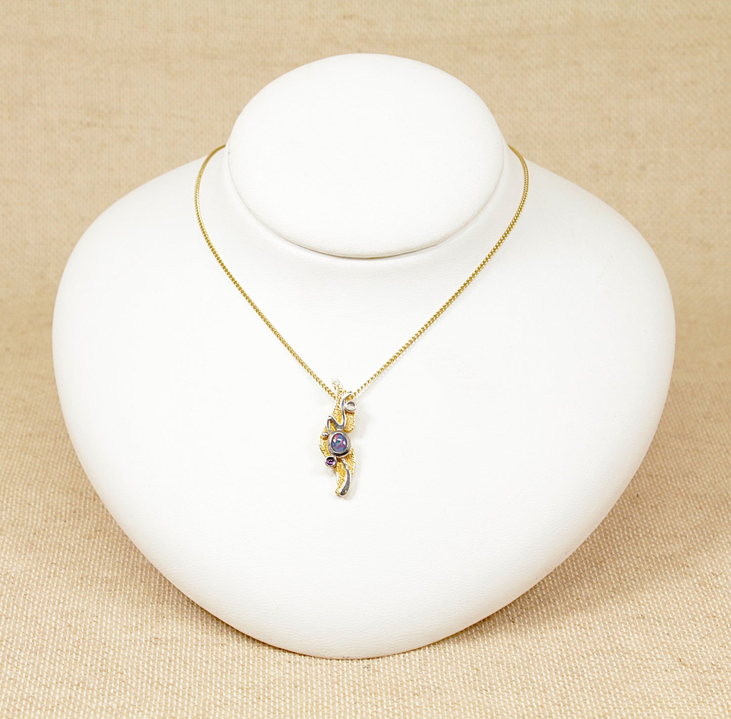 This beautiful 9ct Gold ‘Studio’ design piece from the 1970’s was handcrafted with an emphasis on artistry and originality, the pendant crafted in 9ct Gold has a vibrant Opal that flashes blues, reds and orange, sitting in the centre of the pendant with accented cabochon cut Amethyst and Moonstone gemstones.