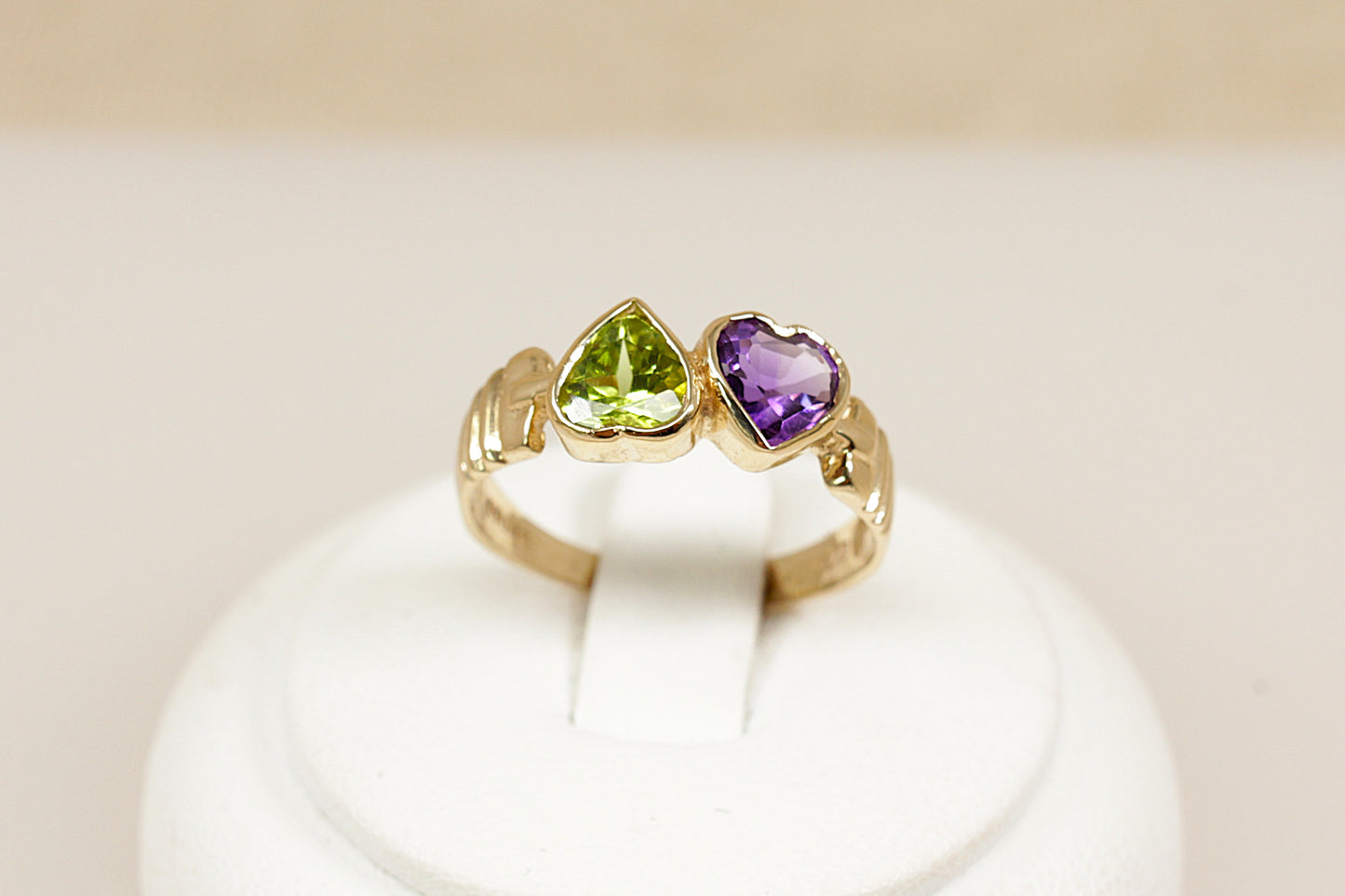 A delightful and symbolic 9ct gold ring, designed as a duo of bezel-set heart-shaped gemstones—a vibrant Peridot and a rich Amethyst, sitting side by side in perfect harmony. The design carries a romantic charm with a bold, confident presence, blending playful colour with classic elegance, UK finger size N.