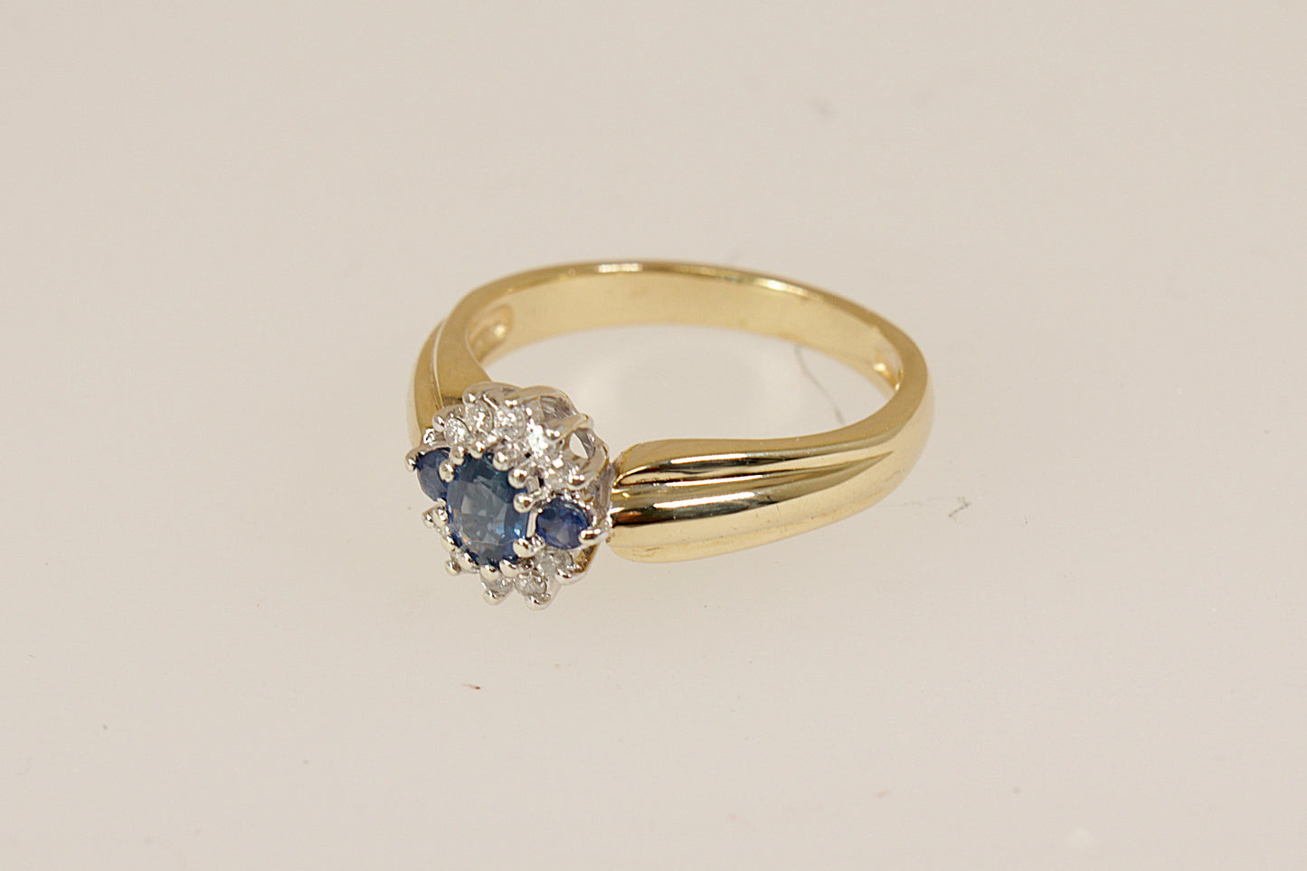 9ct Gold Sapphire and Diamond Cluster Ring, A beautiful and distinctive 9ct Gold ring, showcasing an interesting and elegant design. At its heart is a vibrant oval Blue Sapphire, flanked by two round Blue Sapphires, forming a rich and regal trilogy centrepiece. it bears full London hallmarks for 1993, confirming its gold purity and vintage authenticity, perfect as a unique engagement ring, UK Finger size: O.