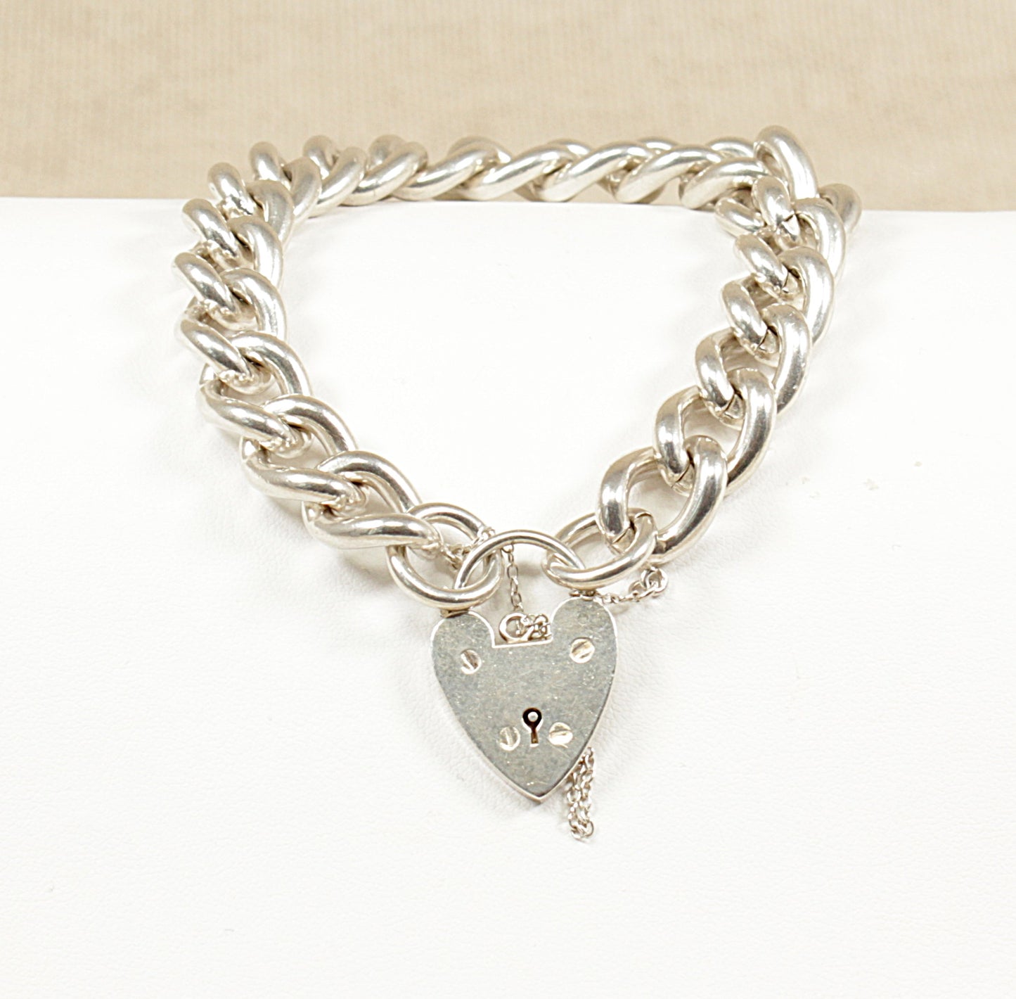 A vintage silver curb link bracelet with a padlock clasp, displayed against a beige background.