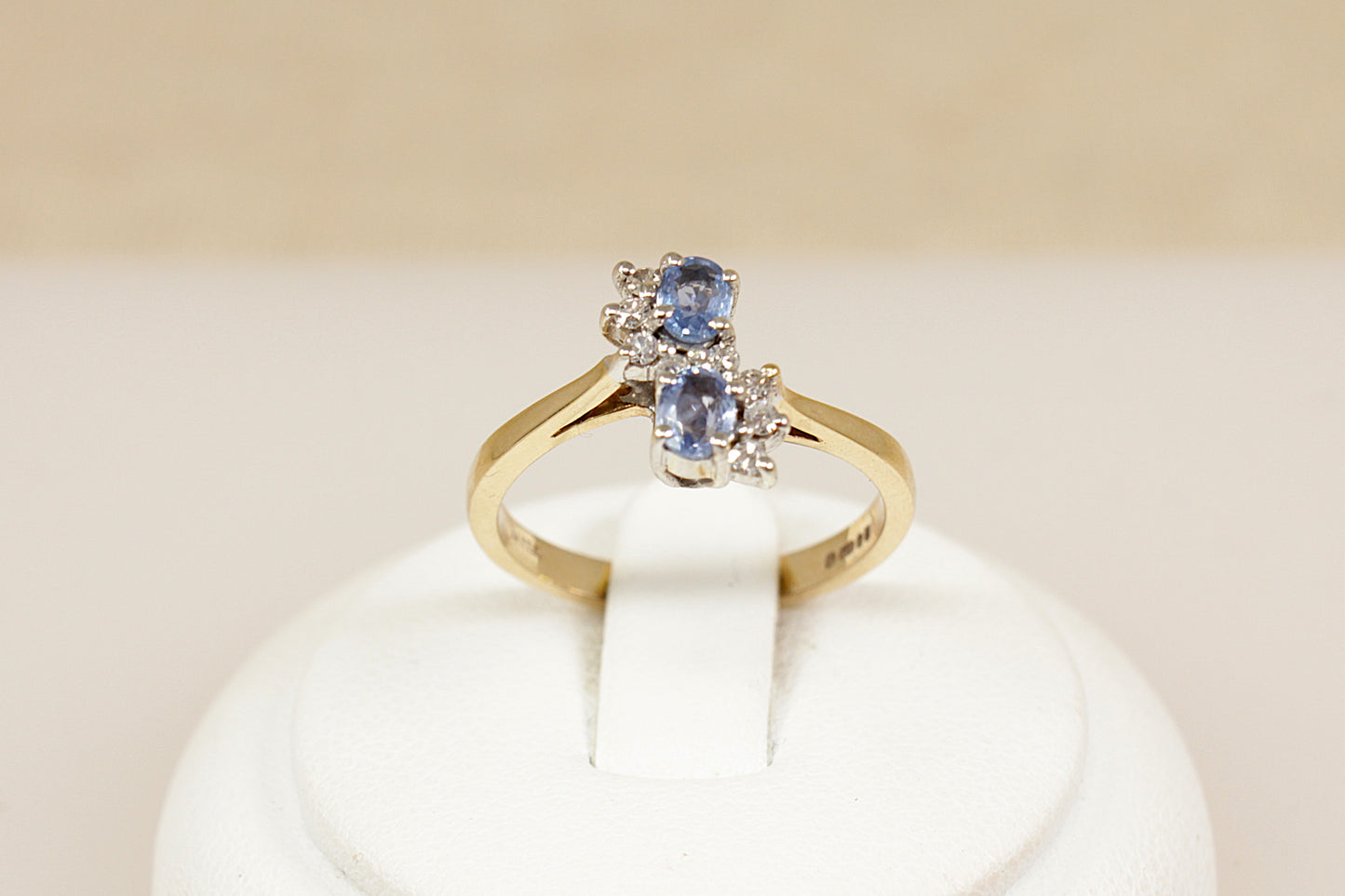 A beautifully designed 9ct gold ring, featuring two oval blue topaz gemstones set vertically with a slight twist, creating a fluid and elegant silhouette. Surrounding the topaz stones are eight sparkling diamonds, gracefully arranged in a flowing S-shape, adding a delicate brilliance and movement to the design, London 1992, UK finger size M.