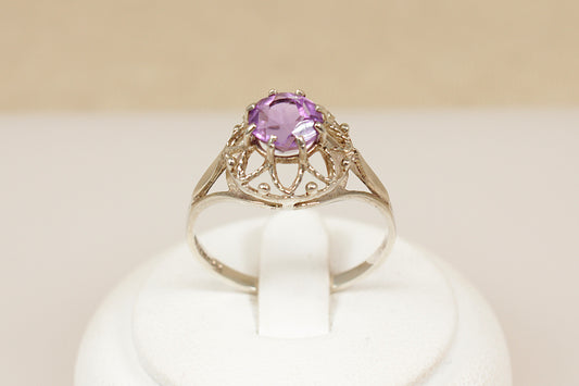 Gold ring with a purple gemstone on a white cushion
