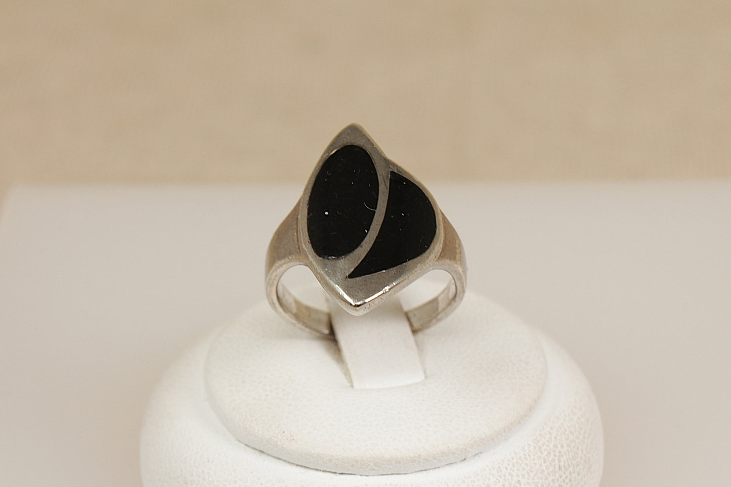 Silver statement ring with black inlay on a white display stand with a beige background