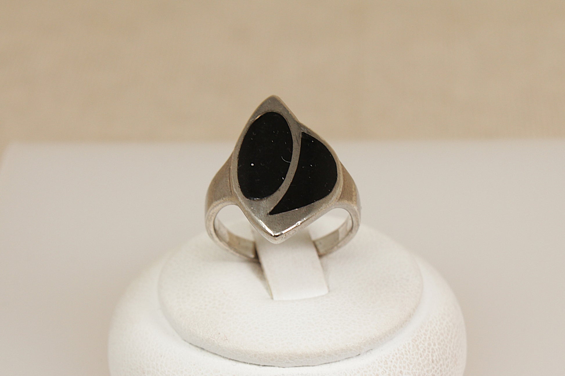 Silver statement ring with black inlay on a white display stand with a beige background