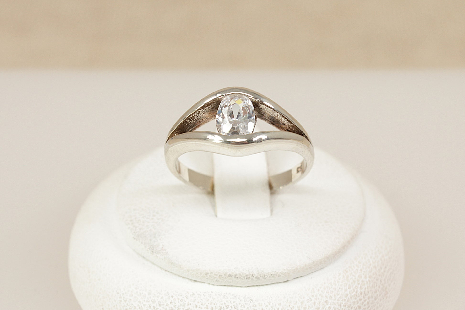 Silver solitaire ring with a cubic zirconia gemstone on a white stand against a beige background