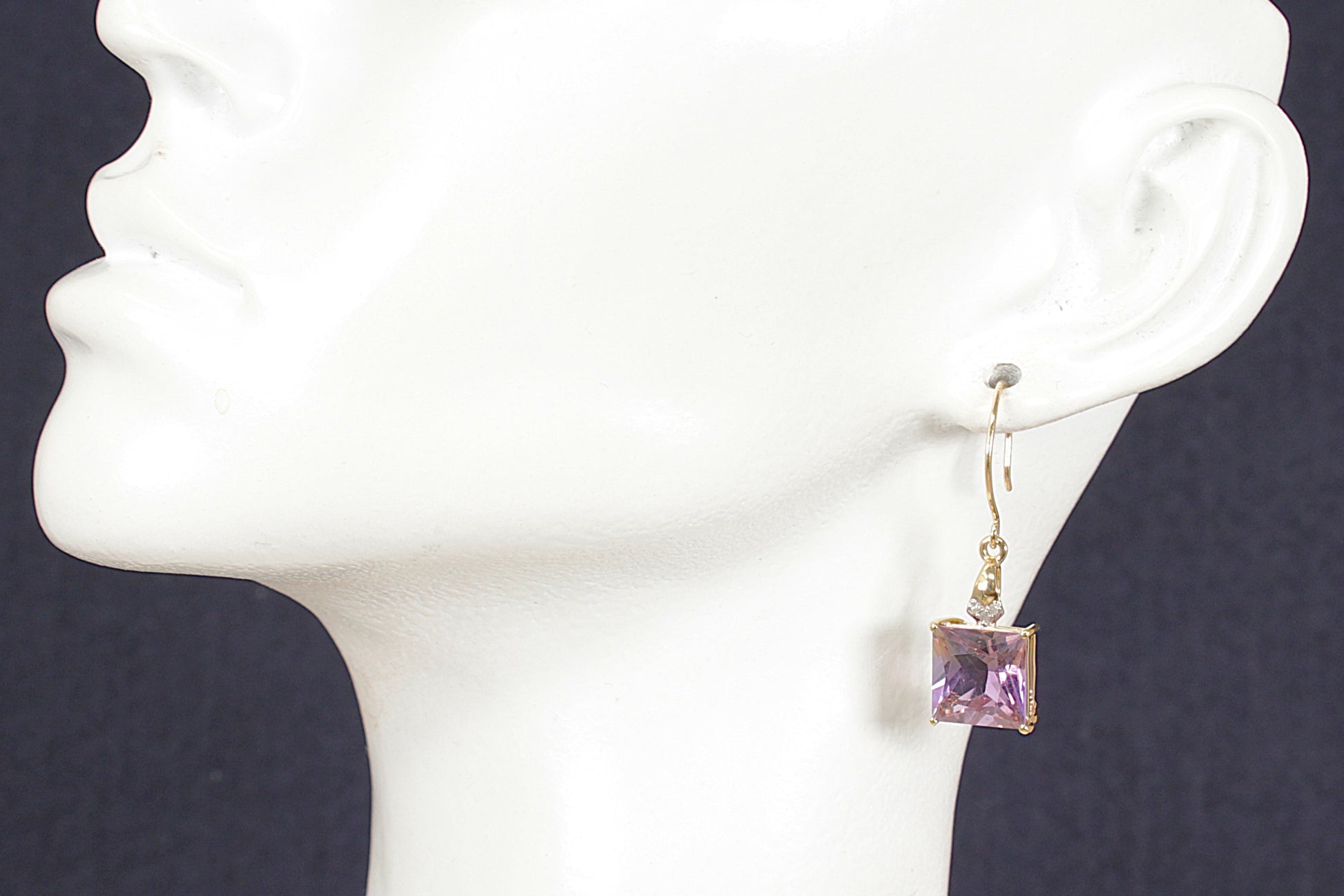 Gold earrings with purple amethyst and diamond gemstones on a white mannequin head against a dark background