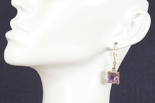 Gold earrings with purple amethyst and diamond gemstones on a white mannequin head against a dark background