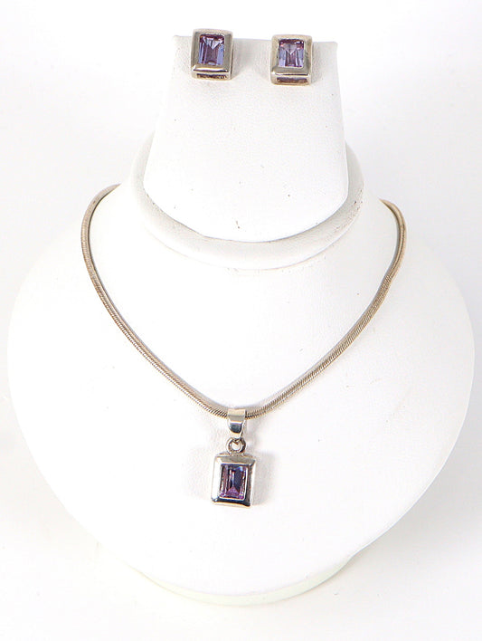 A sterling silver necklace with a square amethyst-colored crystal pendant, accompanied by a matching pair of earrings.