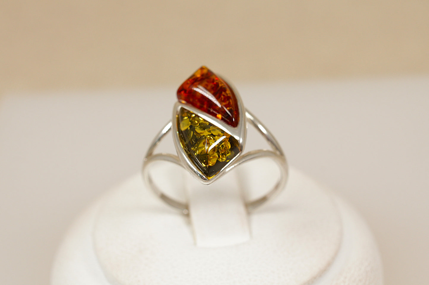 Ring with a multicolored amber gemstone on a white stand against a beige background