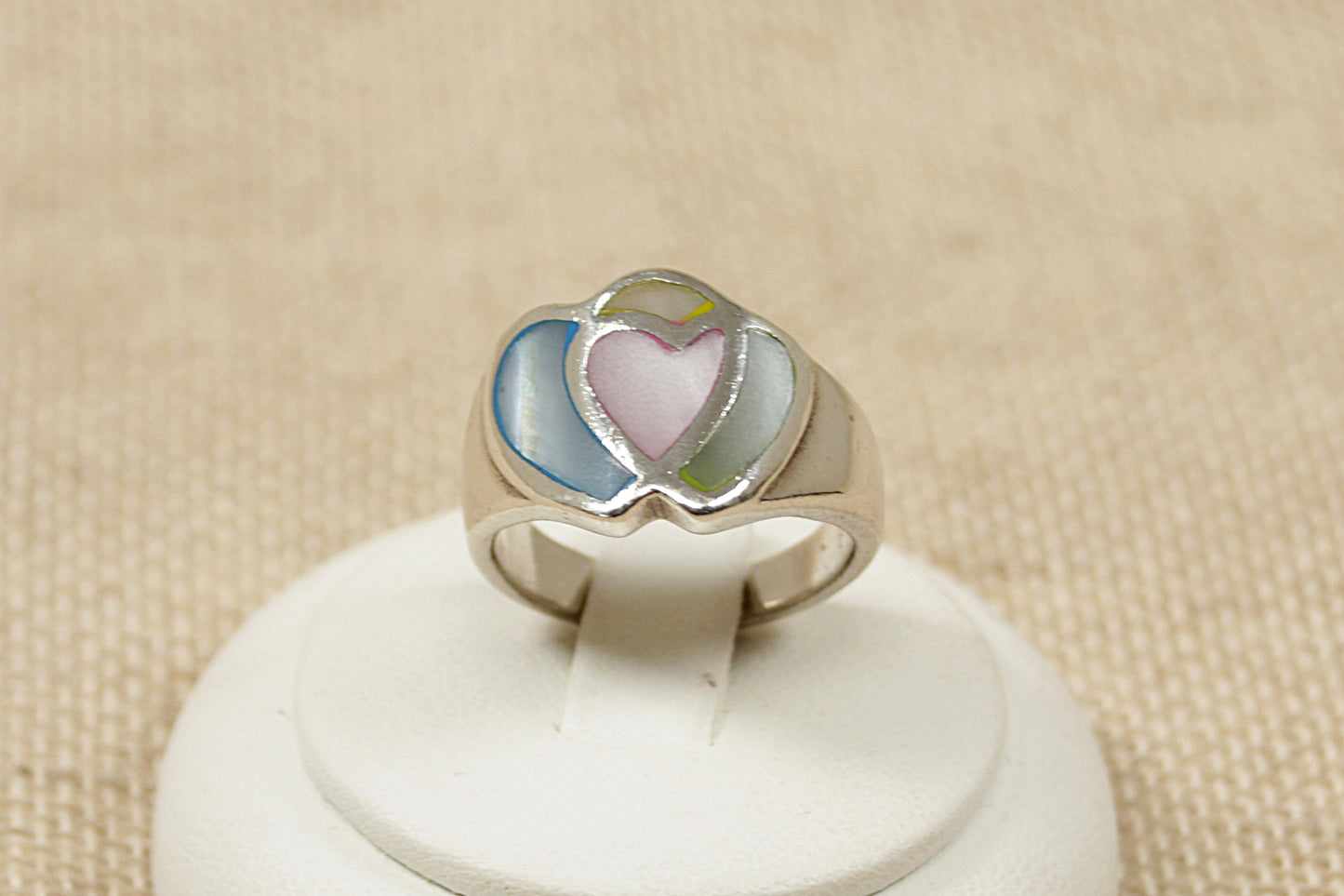 A sterling silver ring with pink and blue mother of pearl inlay in the shape of two hearts, displayed on a white stand.