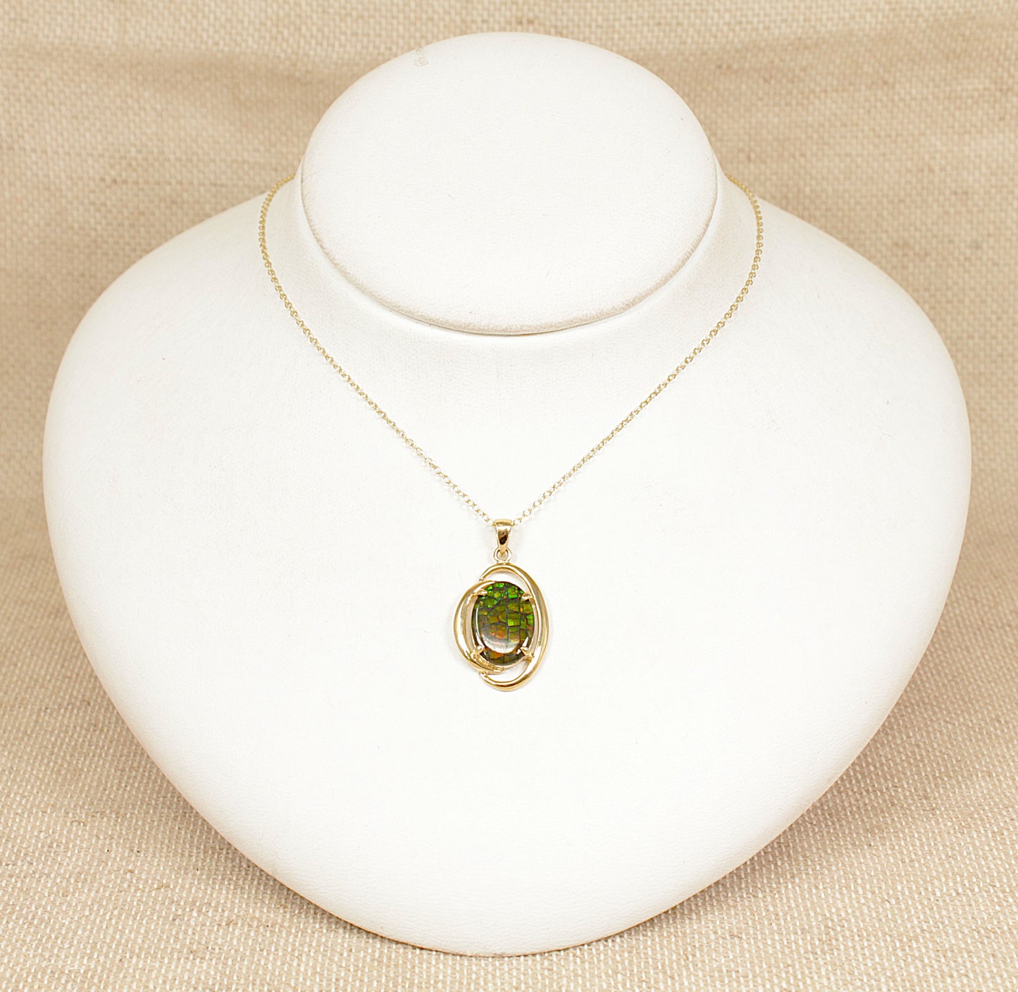 Gold necklace with a opal pendant on a white mannequin bust against a beige background