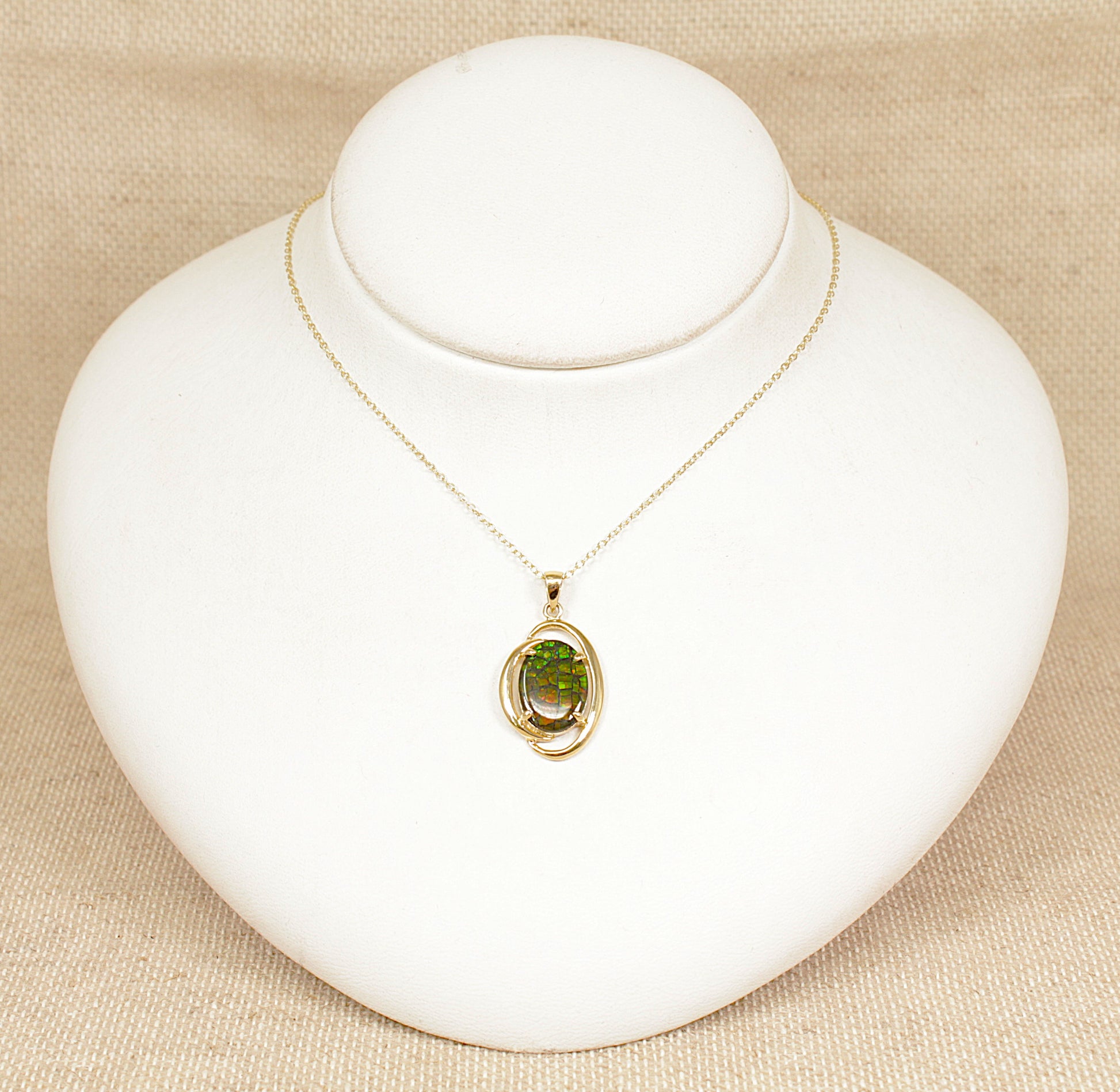 Gold necklace with a opal pendant on a white mannequin bust against a beige background