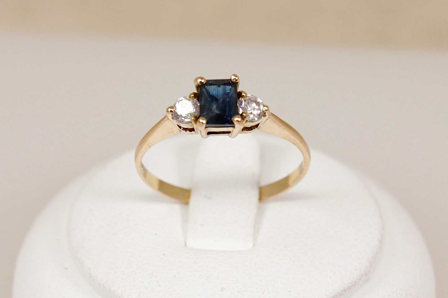Gold ring with a blue sapphire gemstone and two white cz cubic zirconia gemstones on a white stand.