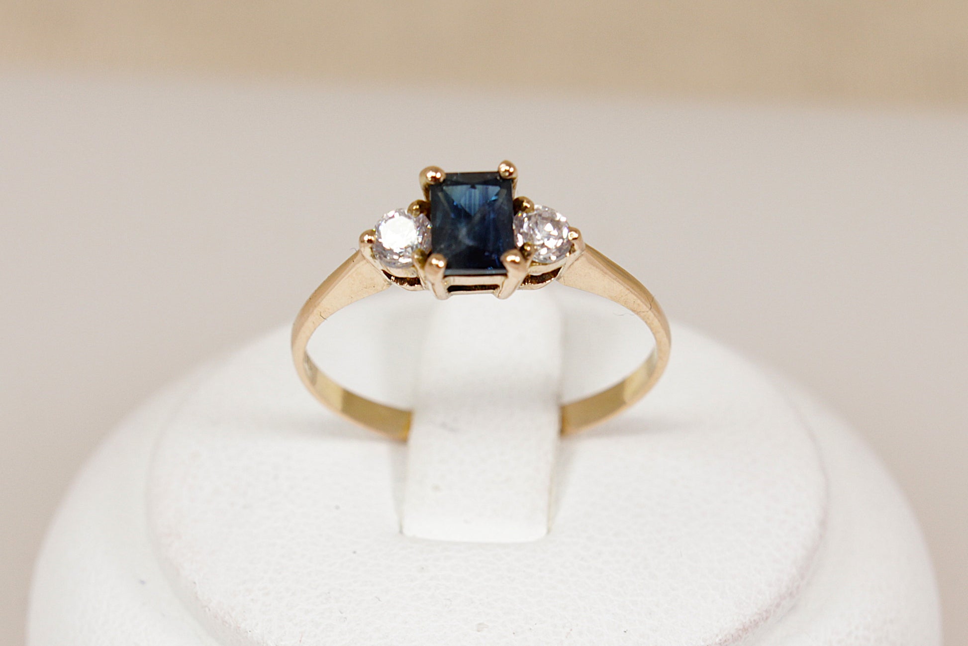 Gold ring with a blue sapphire gemstone and two white cz cubic zirconia gemstones on a white stand.