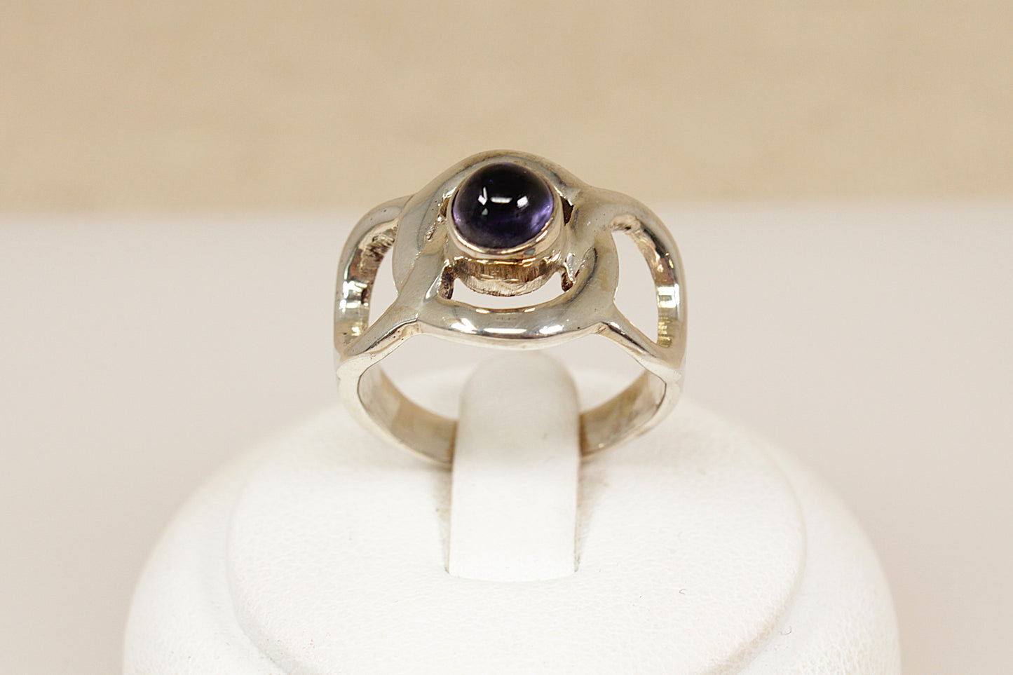Silver ring with a purple gemstone on a white stand against a beige background