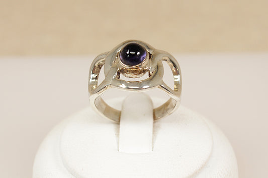 Silver ring with a purple gemstone on a white stand against a beige background