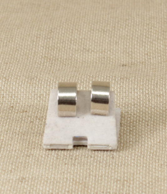 A pair of silver clip-on earrings placed on a beige surface.