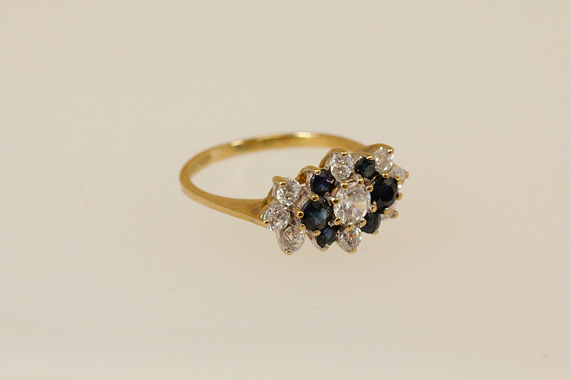 Gold ring with blue and white gemstones on a beige background