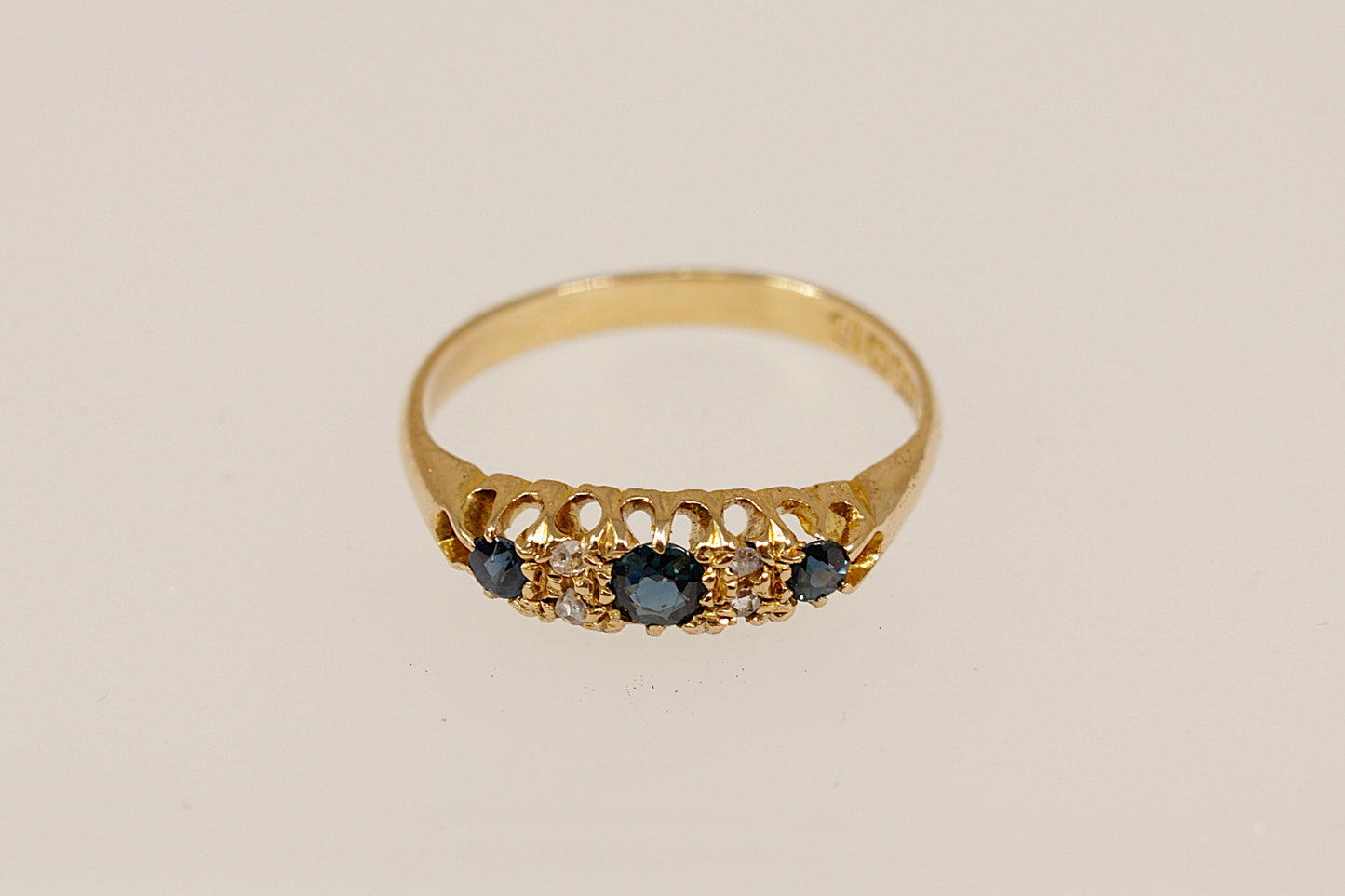 Gold ring with blue sapphire and diamond gemstones on a beige background