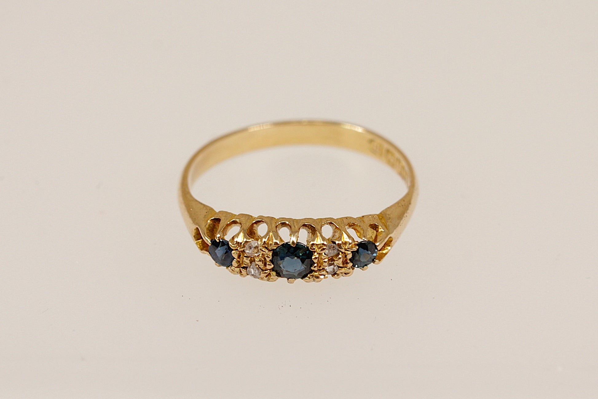 Gold ring with blue sapphire and diamond gemstones on a beige background