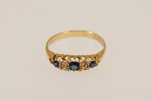 Gold ring with blue sapphire and diamond gemstones on a beige background