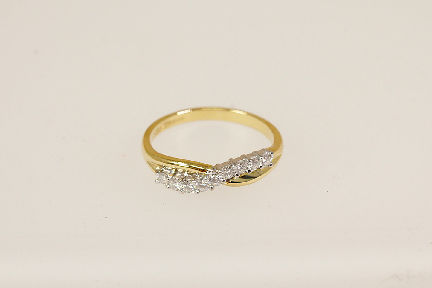 This beautifully crafted 18ct gold half eternity ring features a graceful crossover design, forming a soft wave or 'S' shape that flows elegantly across the finger. Set with nine round brilliant-cut diamonds. The inside of the band the ring has Birmingham assay marks for 18ct gold, along with the date letter for 1994. UK finger size O.