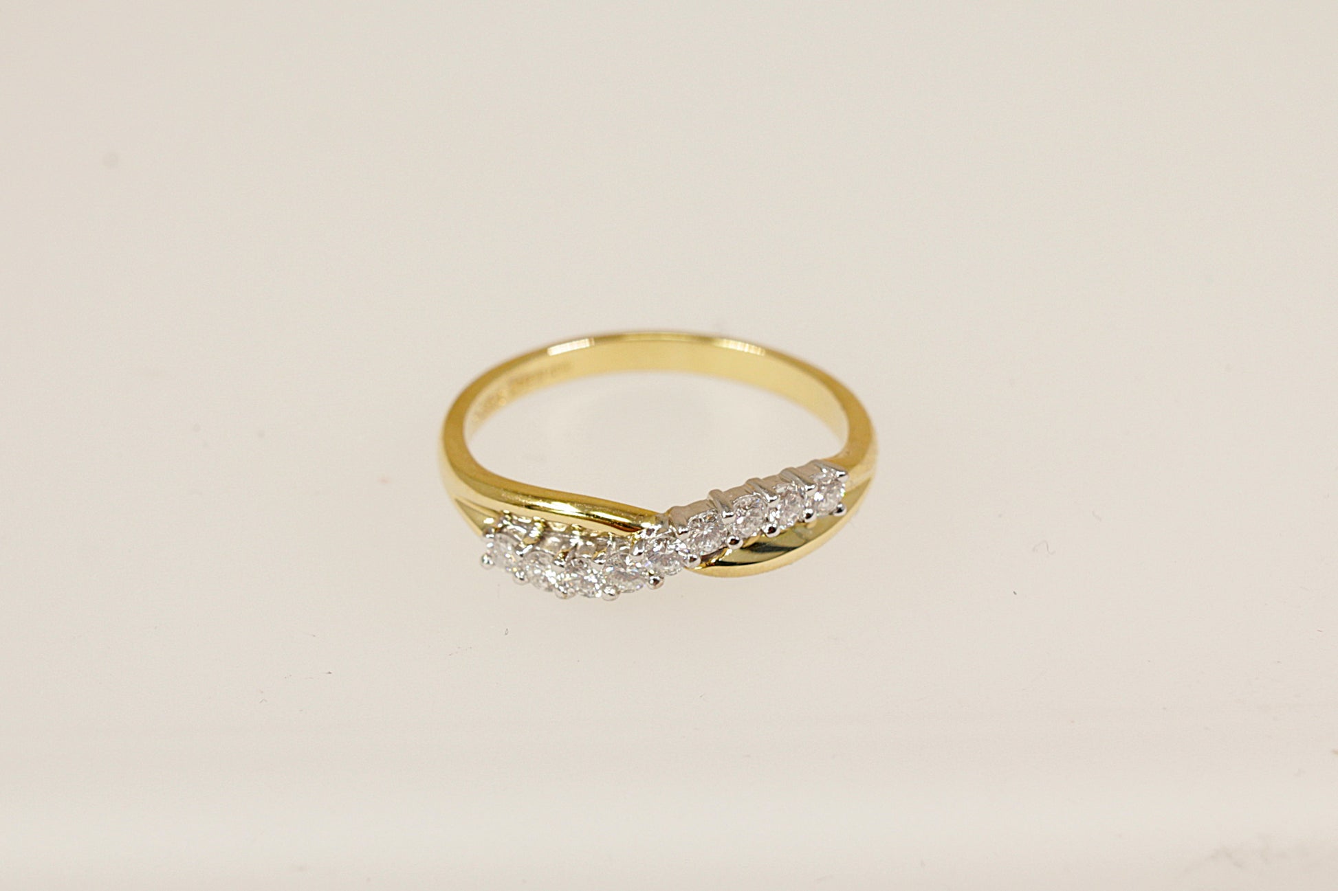 This beautifully crafted 18ct gold half eternity ring features a graceful crossover design, forming a soft wave or 'S' shape that flows elegantly across the finger. Set with nine round brilliant-cut diamonds. The inside of the band the ring has Birmingham assay marks for 18ct gold, along with the date letter for 1994. UK finger size O.