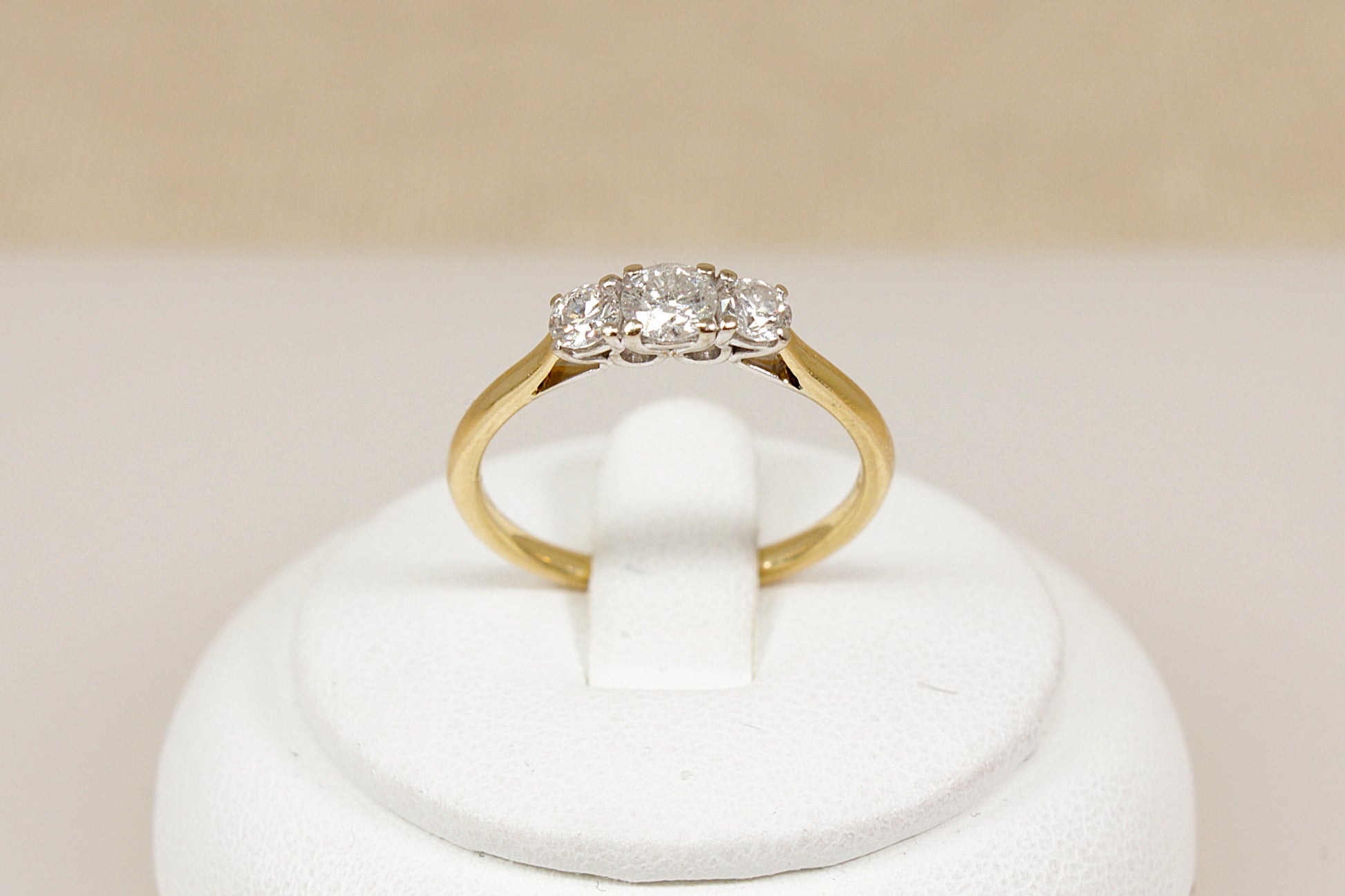 18ct yellow gold ring with diamonds on a white stand against a beige background