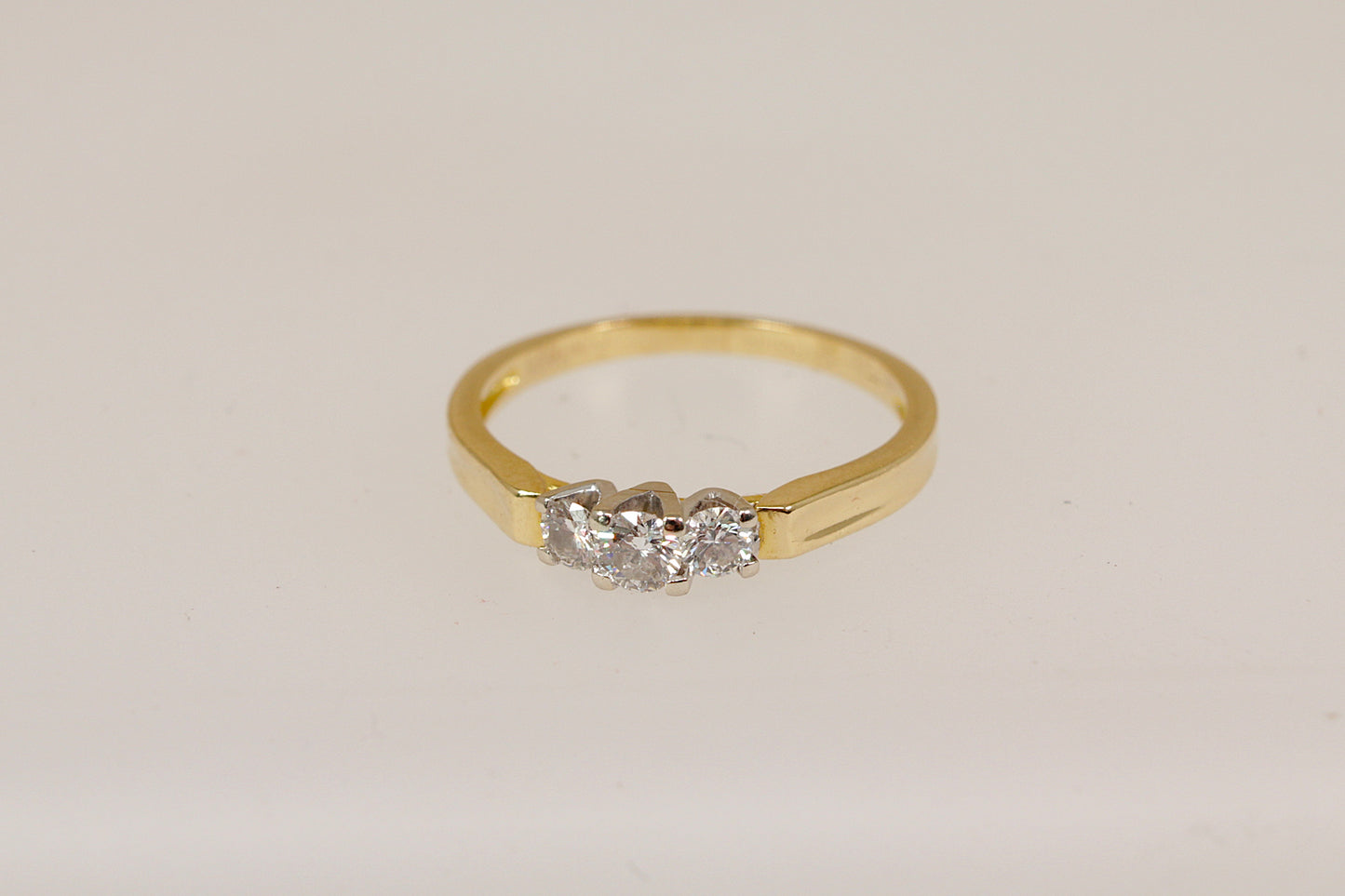 18ct Gold trilogy ring with three diamonds on a light beige background