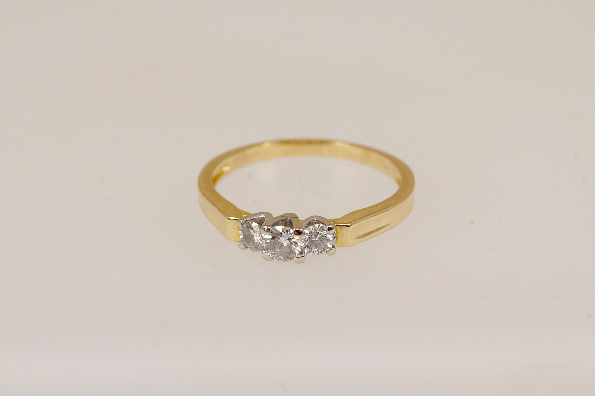18ct Gold trilogy ring with three diamonds on a light beige background