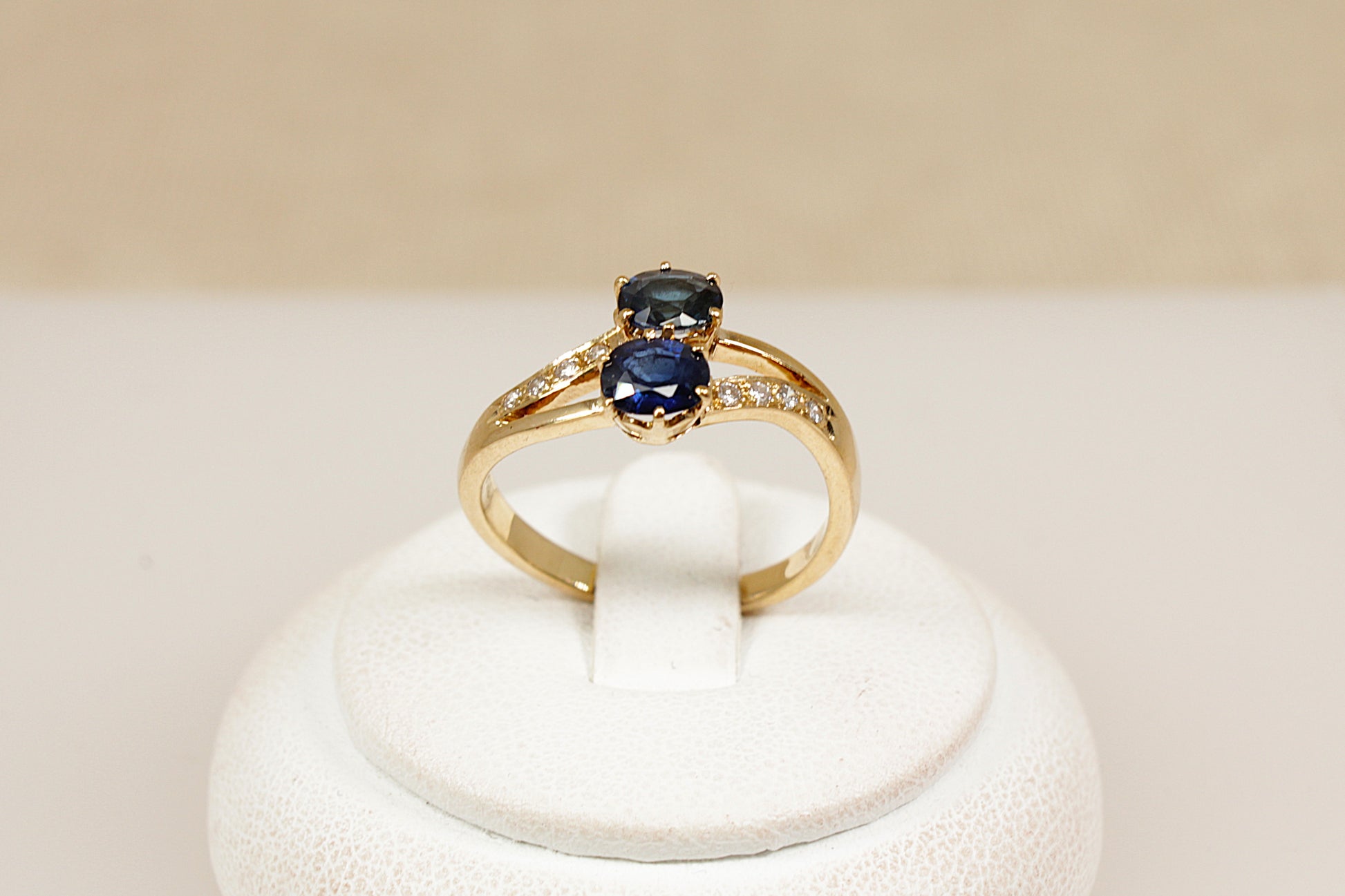 A timeless and romantic design, this 18ct gold ‘Duo’ ring features two round-cut midnight blue sapphires, securely claw-set side by side in a crown-style, split-head setting. The sapphires are positioned on a subtle twist, Each shoulder is adorned with four sparkling diamond accents, adding delicate brilliance and enhancing the ring’s refined elegance. The band is stamped ‘750’ for 18ct gold. UK finger size O.