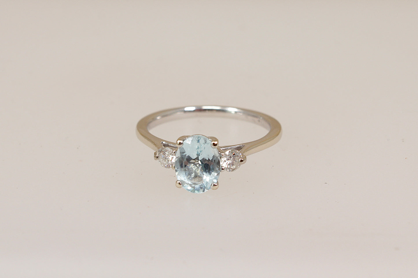 18ct white gold trilogy ring with a blue aquamarine and diamond  gemstones on a beige background