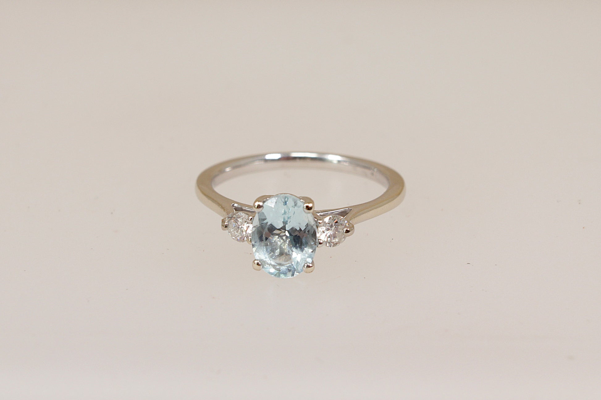 18ct white gold trilogy ring with a blue aquamarine and diamond  gemstones on a beige background