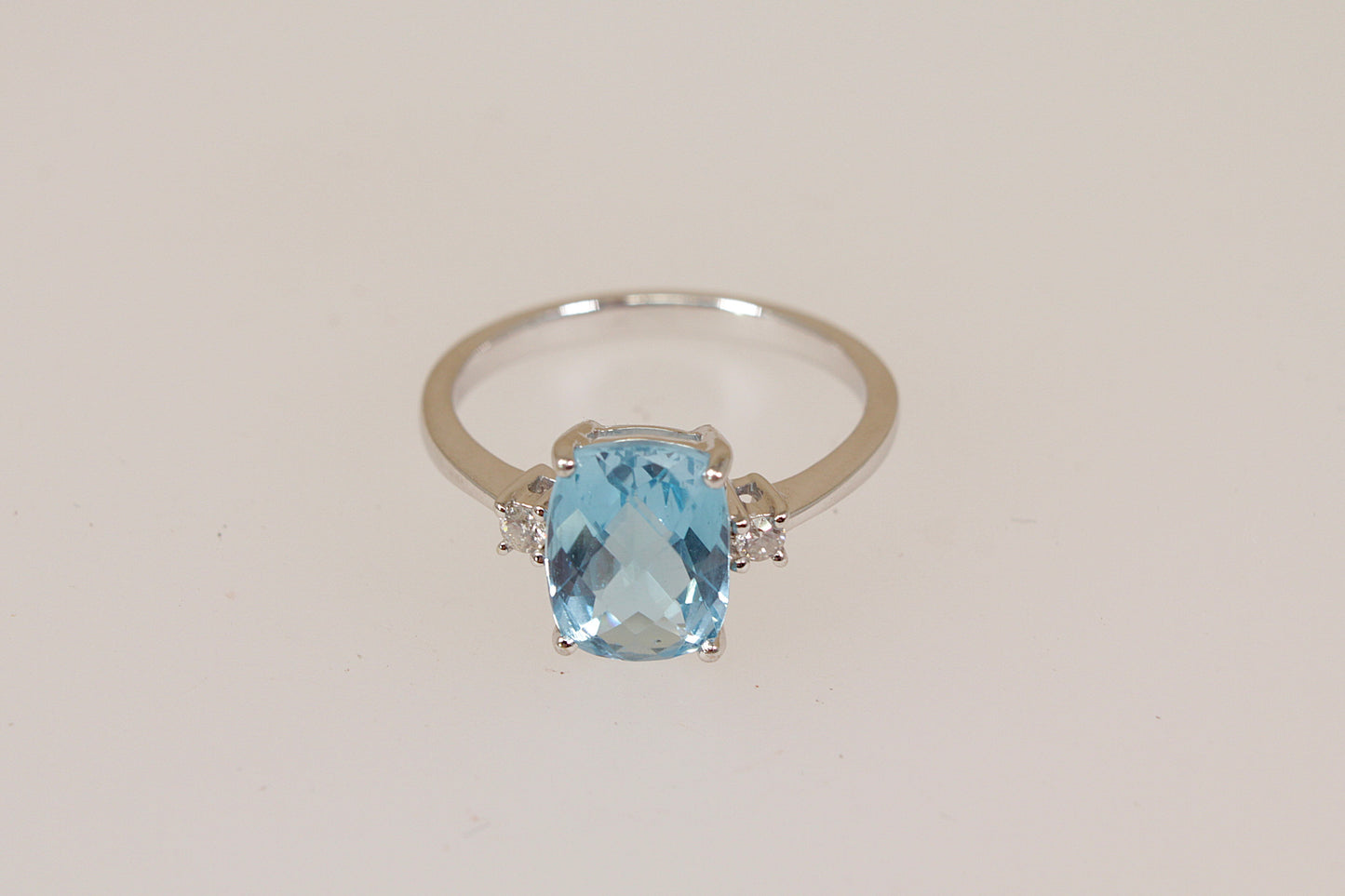 White 18ct gold ring with a blue topaz and white diamond gemstones on a light beige background