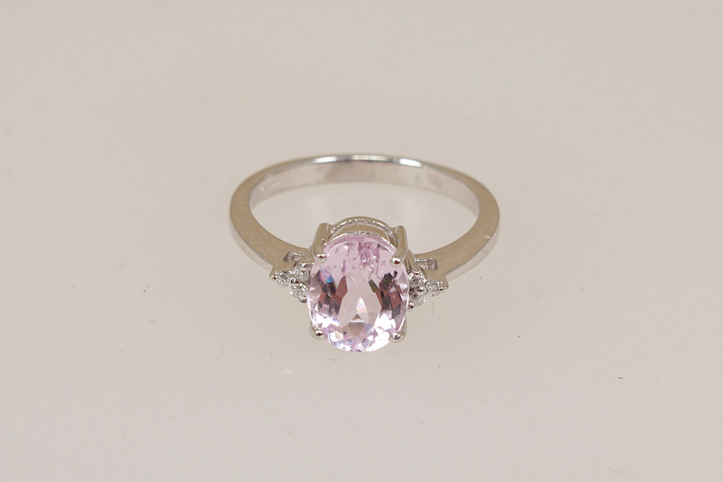 White 18ct gold ring with a pink Kunzite gemstone with diamond accents on a light beige background