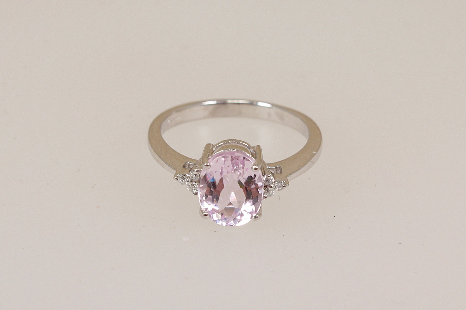 White 18ct gold ring with a pink Kunzite gemstone with diamond accents on a light beige background